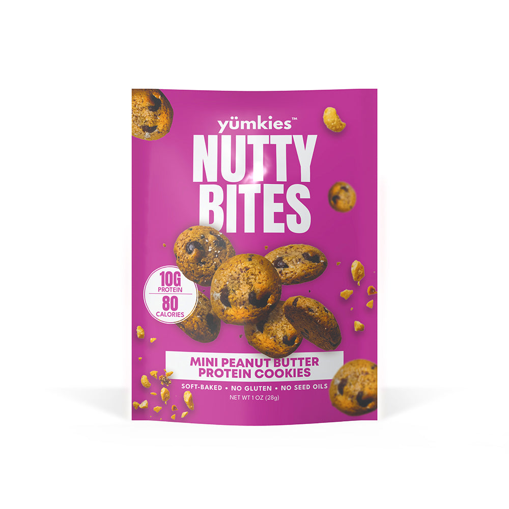 A package of yümkies Nutty Bites Mini Peanut Butter Protein Cookies on a solid white background. The packaging is bright magenta pink with white text and illustrations of the cookies.